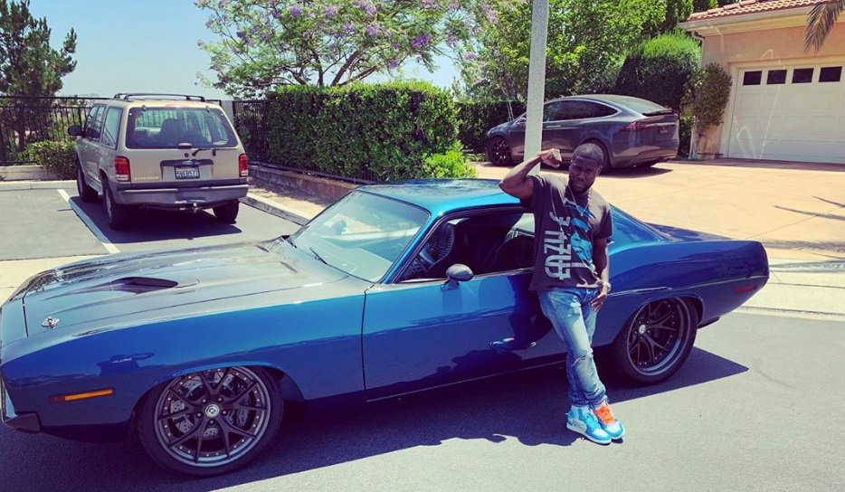 Kevin Hart posing in front of his 1970 Plymoth Barracuda